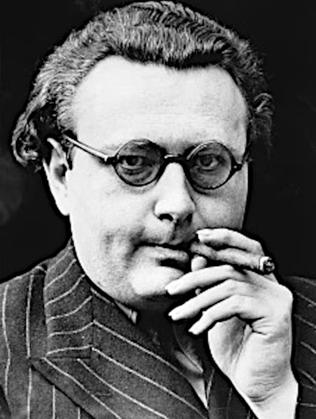A close-up black and white portrait of astrologer Louis de Wohl. He is facing forward, wearing round, dark-rimmed spectacles and a pinstriped suit jacket. His right hand is raised near his face, holding a burning cigar between his fingers, and he has a focused, intense gaze directed into the camera.
