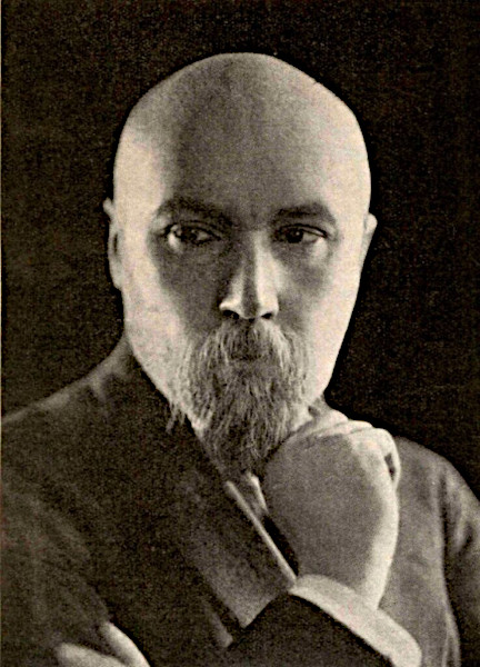 A sepia-toned vintage portrait photograph of Nicholas Roerich. The subject is a bald man with a prominent beard and mustache, resting his chin thoughtfully on his hand while staring directly forward into the camera with an intense expression.