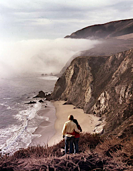 A 1960s color photograph of a young couple looking out over the ocean from the hills of Big Sur California
