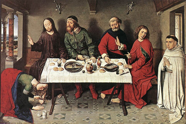 An oil painting depicting five figures gathered around a long table set with fish, bread, and wine in a 15th-century European interior. On the left, a robed Jesus sits with a hand raised in blessing while a woman in a red cloak kneels at his feet, anointing them from a small container. Three other men in medieval European cloaks and hats sit at the table. On the far right, a Roman Catholic monk in white habits stands with hands clasped in prayer, watching the scene.