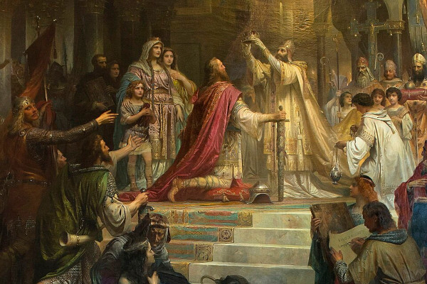 A large classical oil painting depicting a grand coronation ceremony inside a stone cathedral. In the center, a bearded king in a rich red and gold cloak kneels on a raised, carpeted platform. He rests his hand on a large unsheathed sword. A pope in elaborate white and gold liturgical vestments stands above him, holding a golden crown high in the air to place on the king's head. The scene is crowded with onlookers, including royal family members, guards in armor, white-robed altar boys with incense, and other church clergy watching from the background.