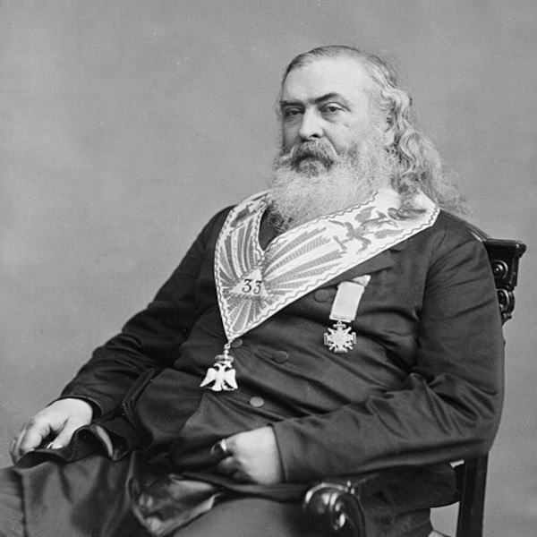 A historical black-and-white portrait photograph of Albert Pike taken by Mathew Brady. He is an older, heavyset man with long, unkempt gray hair flowing past his shoulders and a thick, wild white beard. He wears a heavy dark coat and sits looking slightly away from the camera.