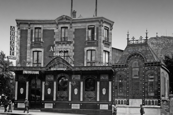 Black and white photograph of l'Abbaye at 1 Place Pigalle in the 1920s, featuring "Abbaye Tango" signage, a dark ornate storefront, and elaborate stained-glass windows.