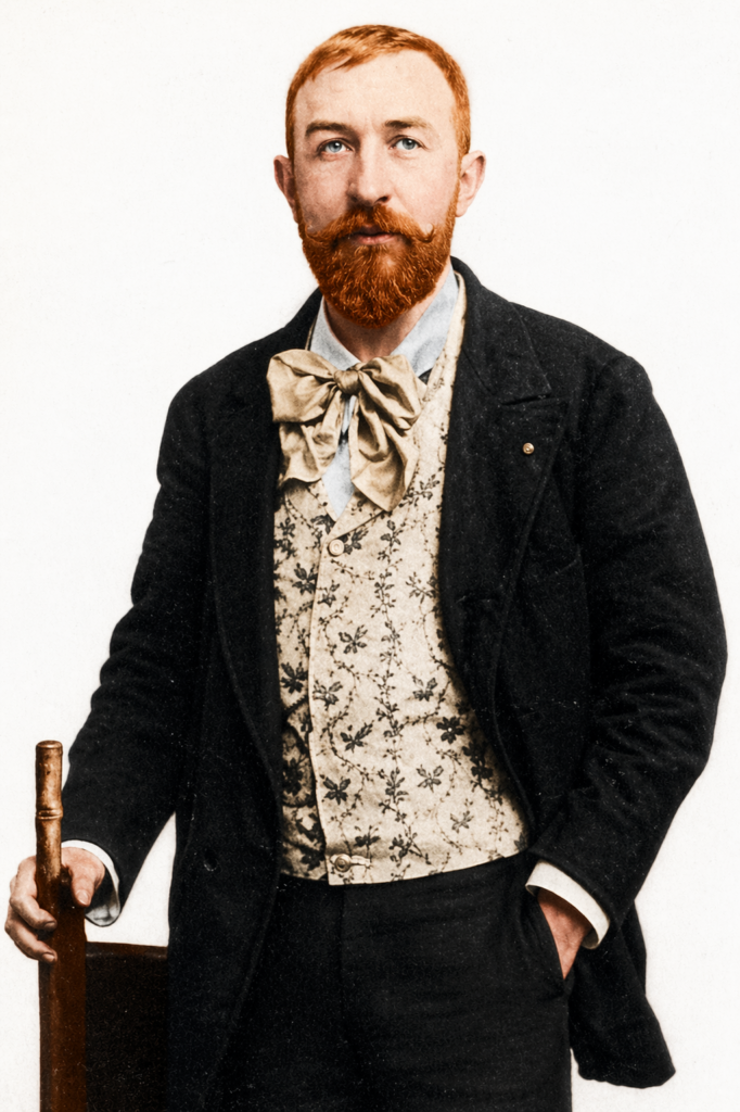 Colorized studio portrait of Rodolphe Salis, founder of Le Chat Noir, featuring his signature red beard, floral waistcoat, and oversized bow tie.