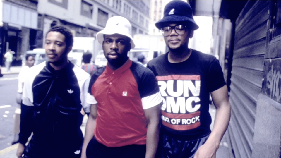 Publicity photograph of the hip hop group Run-DMC posing together on a city street.