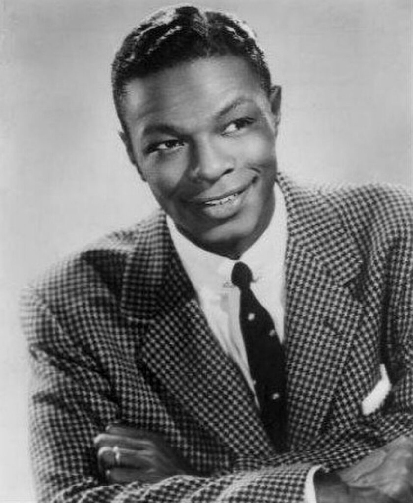 Historic black and white publicity headshot of the legendary singer and jazz pianist Nat King Cole wearing a houndstooth suit jacket and tie.