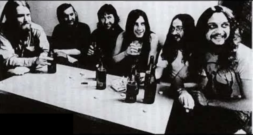 Black and white photo of the band, Plastic People of the Universe sitting around a table.