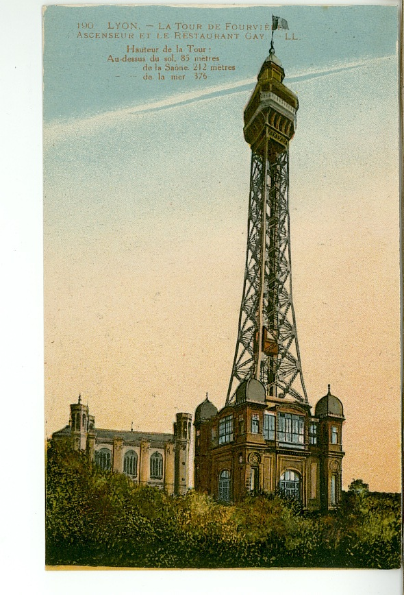 A vintage color-tinted postcard depicting the Metallic Tower of Fourvière rising above a lush green hillside against a pale blue and amber gradient sky. The tower features a massive, open-work steel lattice structure that tapers upward to a viewing platform, a lantern room, and a flying flag at the very peak. The base of the tower is anchored into a multi-story stone pavilion building with rounded windows, glass-enclosed balconies, and small dome-capped corner turrets. To the left, a portion of a stone building with arched windows and small corner spires peeks out from the treetops. French text detailing the tower's height statistics is printed in the upper left corner.