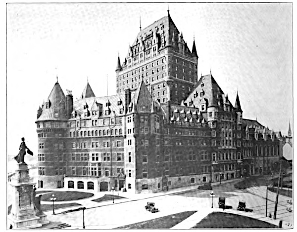 An archival black and white photograph from the early 1900s capturing the massive, fortress-like architecture of the Château Frontenac in Quebec City, showcasing its soaring central tower, steep chateau roofs, and ornate turrets overlooking an empty street with early vintage automobiles parked nearby.