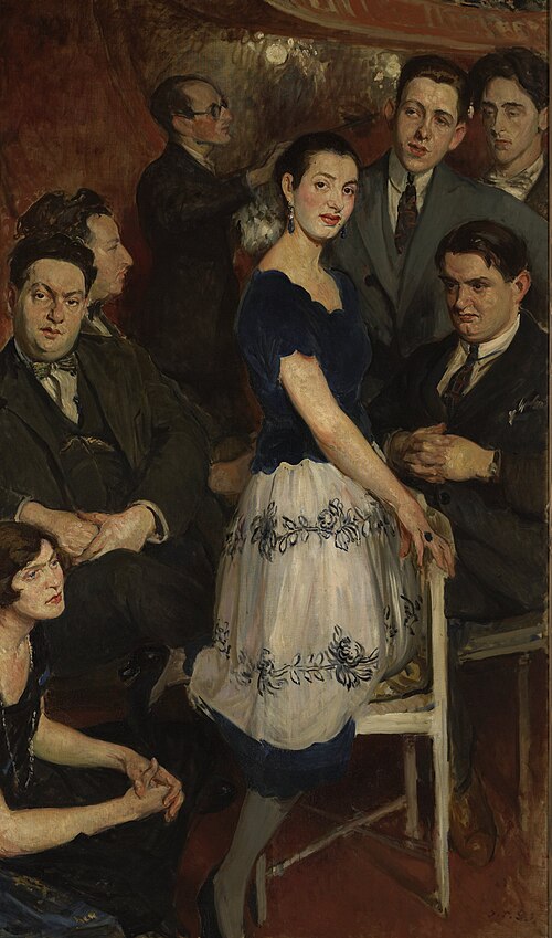 A dark, expressive oil painting depicting a group of modern Parisian artists and musicians inside a theater box. A central woman in a navy blue dress and a patterned white skirt poses dramatically, leaning against a white chair. She is surrounded by several men in formal suits and ties, including a young Jean Cocteau standing in the upper right corner next to a man with closed eyes, and a heavy-set man seated on the left.