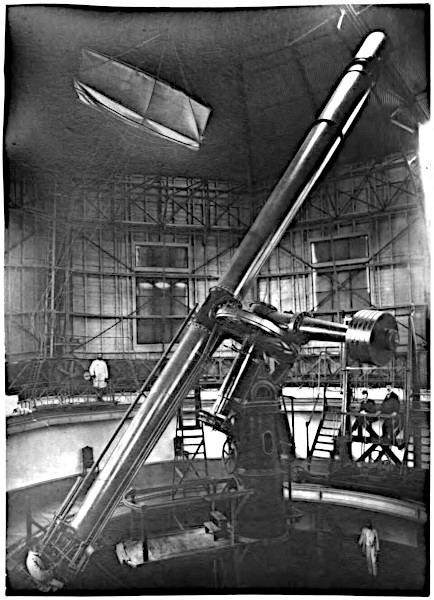 An archival black and white photograph from the late 19th century inside a massive, domed observatory workshop dominated by a giant mechanical refracting telescope on an iron mount, with small human figures standing on surrounding catwalks